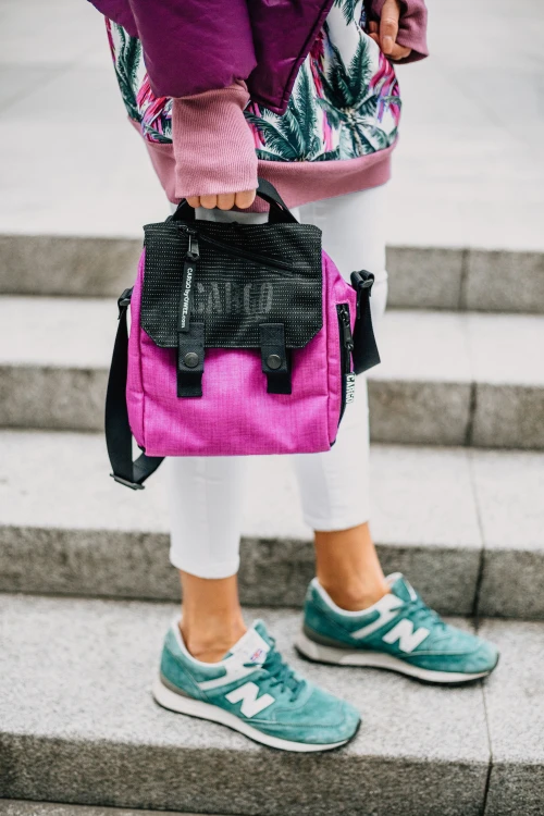 kobieta z małą fioletową magenta odblaskową torbą plecakiem listonoszką miejską na tle miasta
